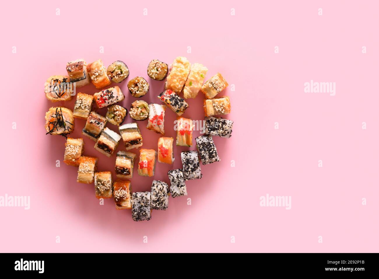 Sushi-Set und Brötchen serviert als Herz auf rosa. Essen zum Valentinstag. Blick von oben. Speicherplatz kopieren. Urlaubslieferung. Stockfoto