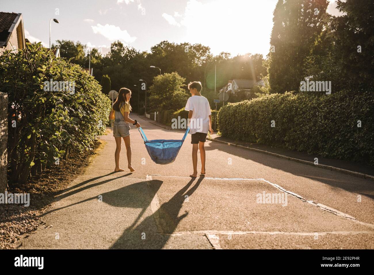 Bruder und Schwester tragen Tasche auf der Straße während sonnigen Tag Stockfoto
