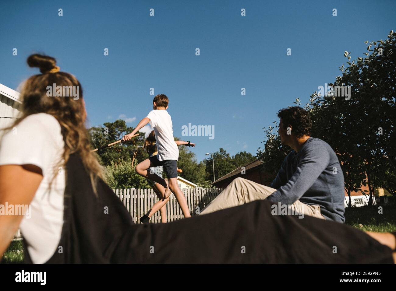 Bruder und Schwester genießen, während Eltern im Hinterhof sitzen An sonnigen Tag Stockfoto