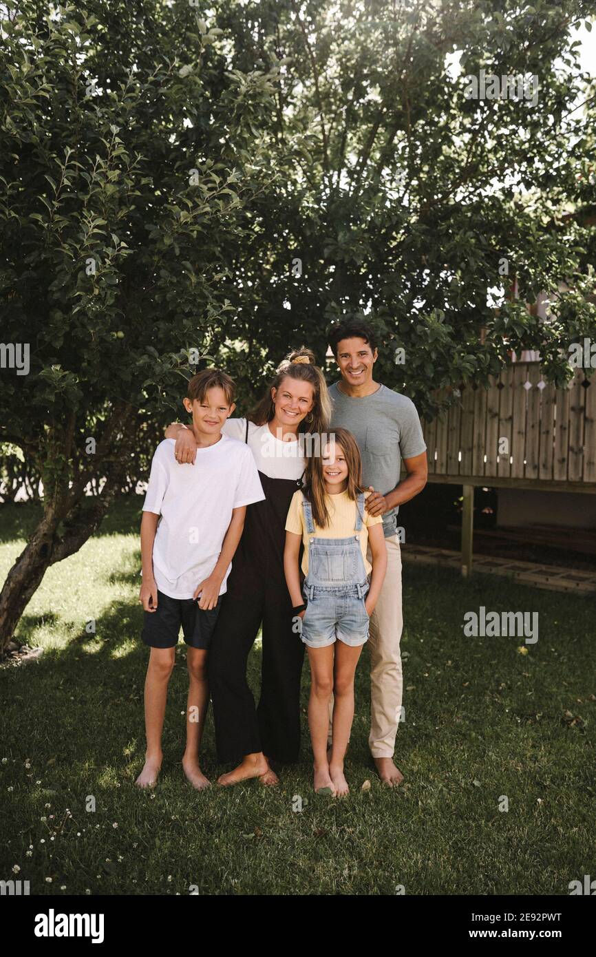 Glückliche Familie steht gegen Baum im Hinterhof Stockfoto