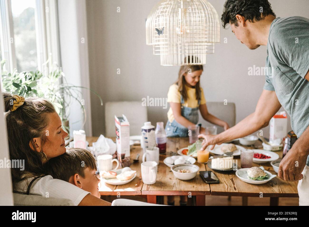 Mutter und Sohn umarmen, während Vater und Tochter stehen Am Esstisch Stockfoto