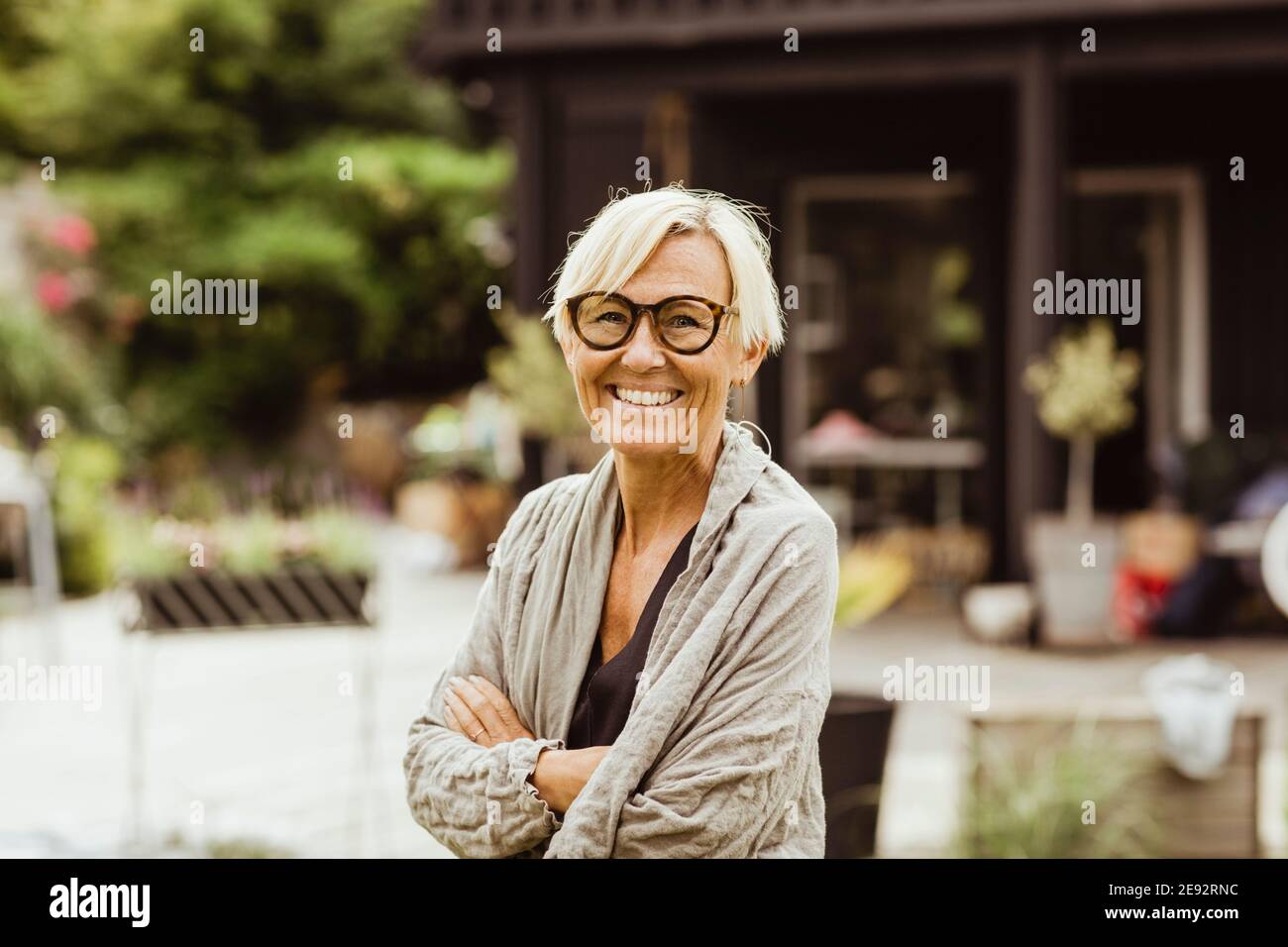 Lächelnde reife Frau mit gekreuzten Armen im Hinterhof Stockfoto