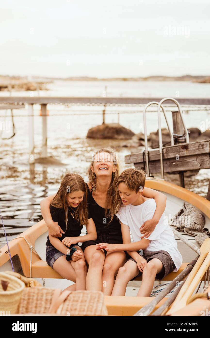 Lächelnde Mutter mit Armen um Kinder, die im Boot sitzen hafen Stockfoto