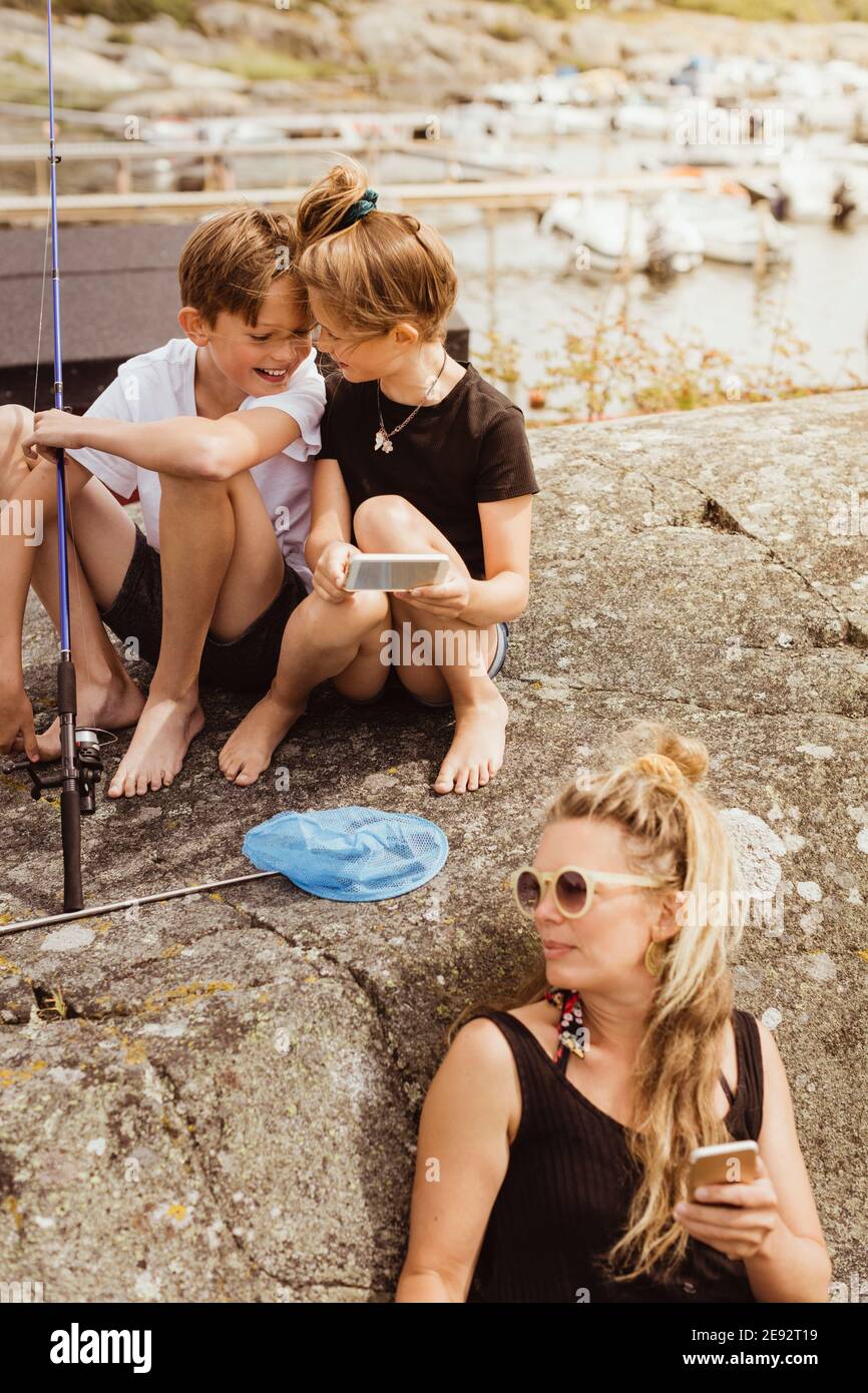 Mutter und Kinder mit Smartphone verbringen Freizeit bei Hafen während des Picknicks Stockfoto