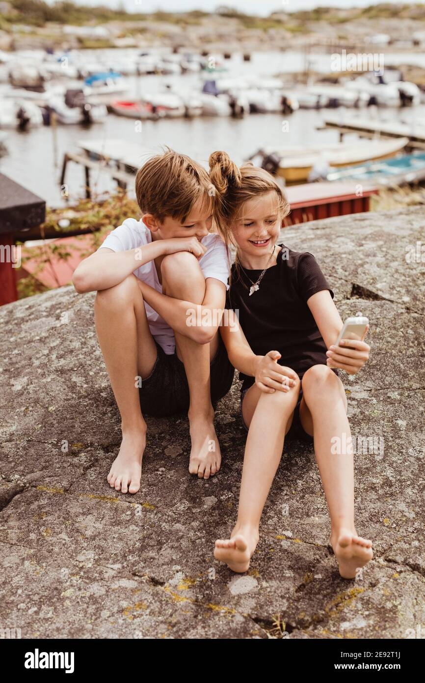 Schwester nimmt Selfie mit Bruder auf Smartphone gegen Hafen Während der Ferien Stockfoto