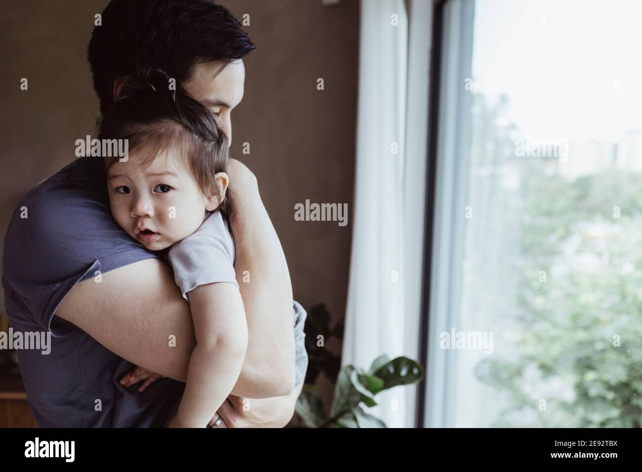 Vater trägt Baby Sohn am Fenster zu Hause Stockfoto