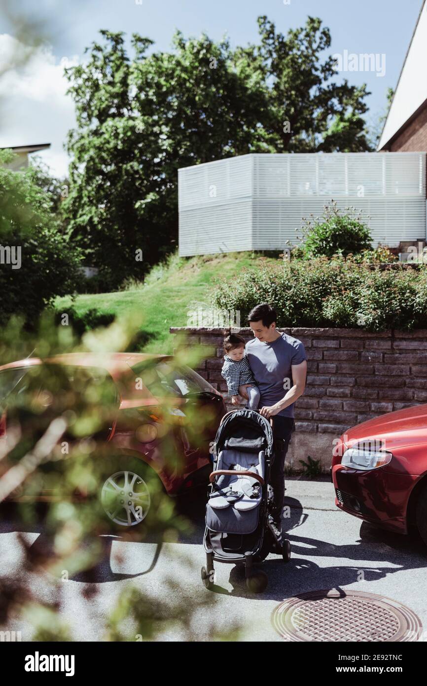 Vater mit Baby Kinderwagen trägt männliche Kleinkind auf der Straße während Sonniger Tag Stockfoto