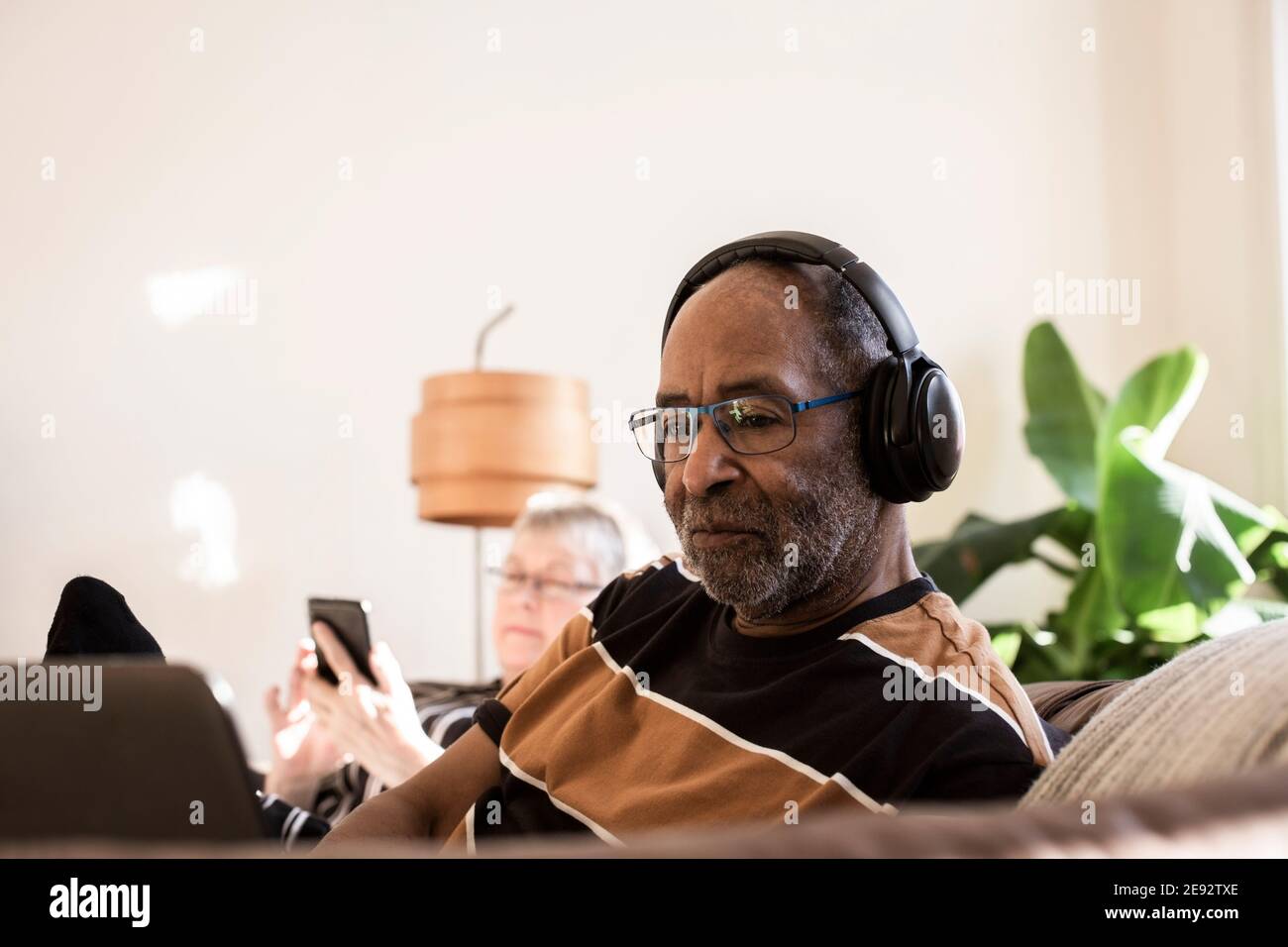 Älterer Mann mit Kopfhörern mit Laptop zu Hause Stockfoto