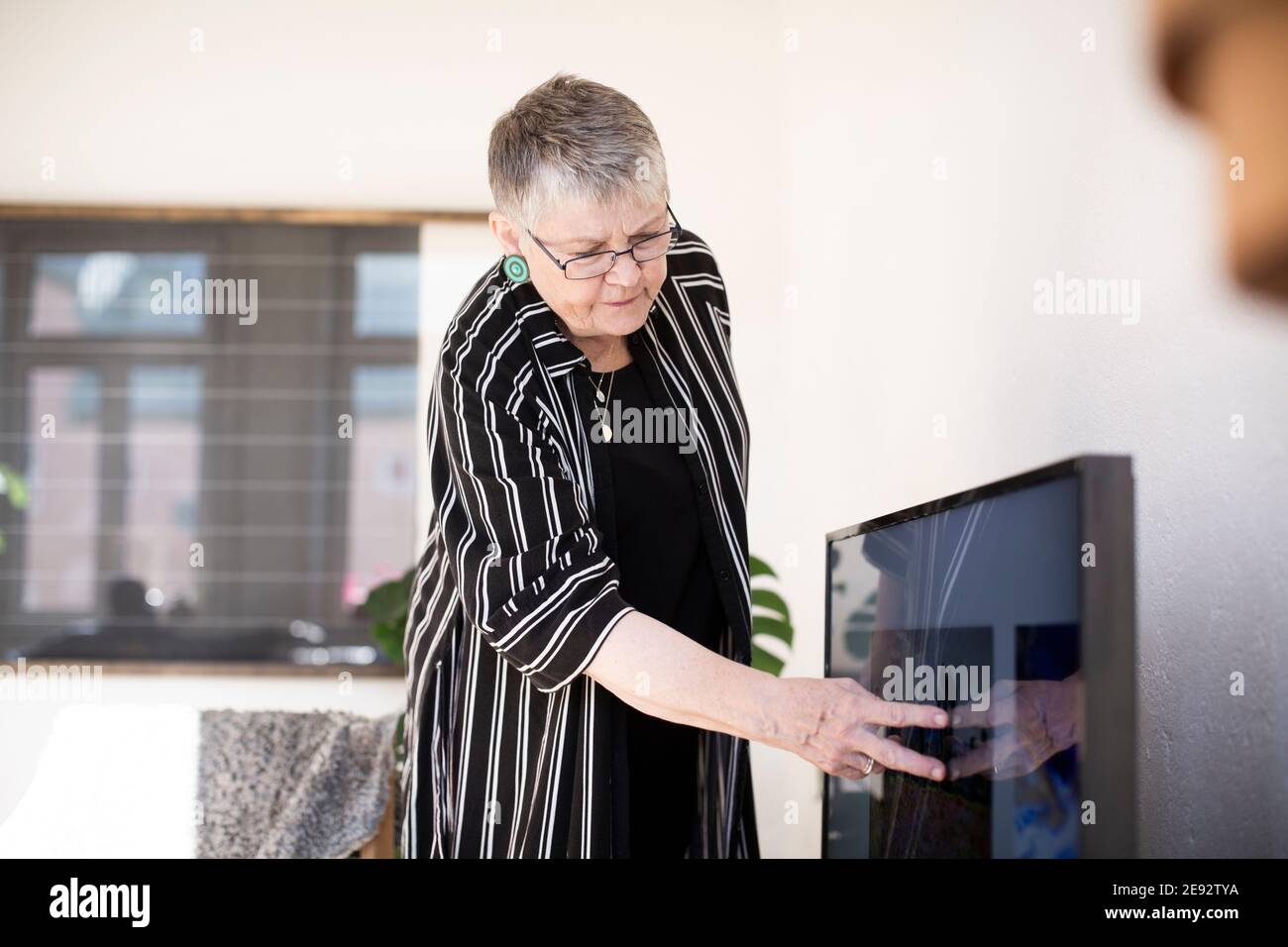 Ältere Frau berührt Fernsehbildschirm im Wohnzimmer Stockfoto