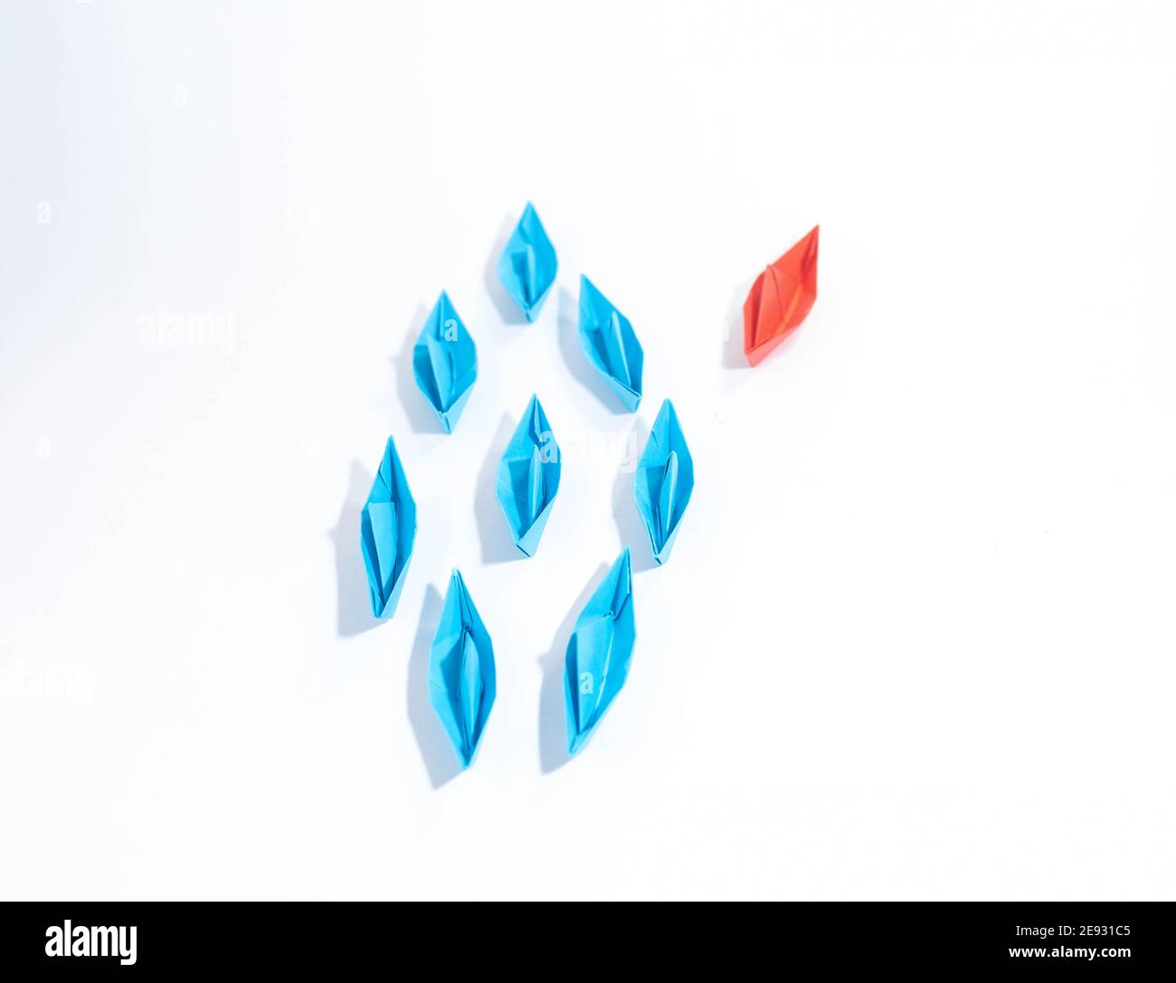 Gruppe von blauen Papierbooten in eine Richtung und ein rotes Papierboot, das unterschiedlich auf weißem Hintergrund zeigt. Business für innovatives Lösungskonzept. Stockfoto