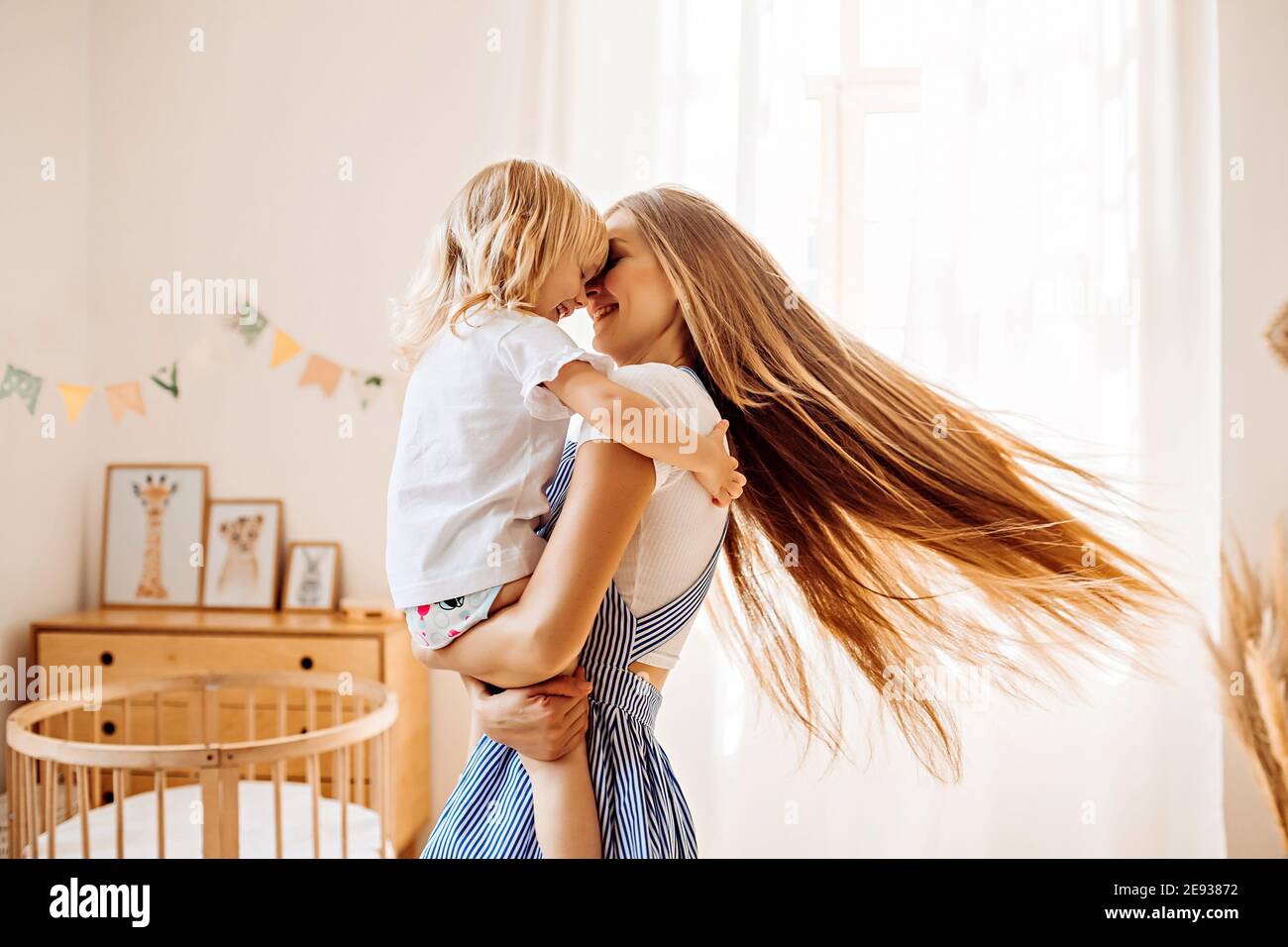 Junge Mutter oder Babysitter mit einem kleinen Mädchen in ihr Die Arme drehen sich in der Mitte des Raumes Stockfoto
