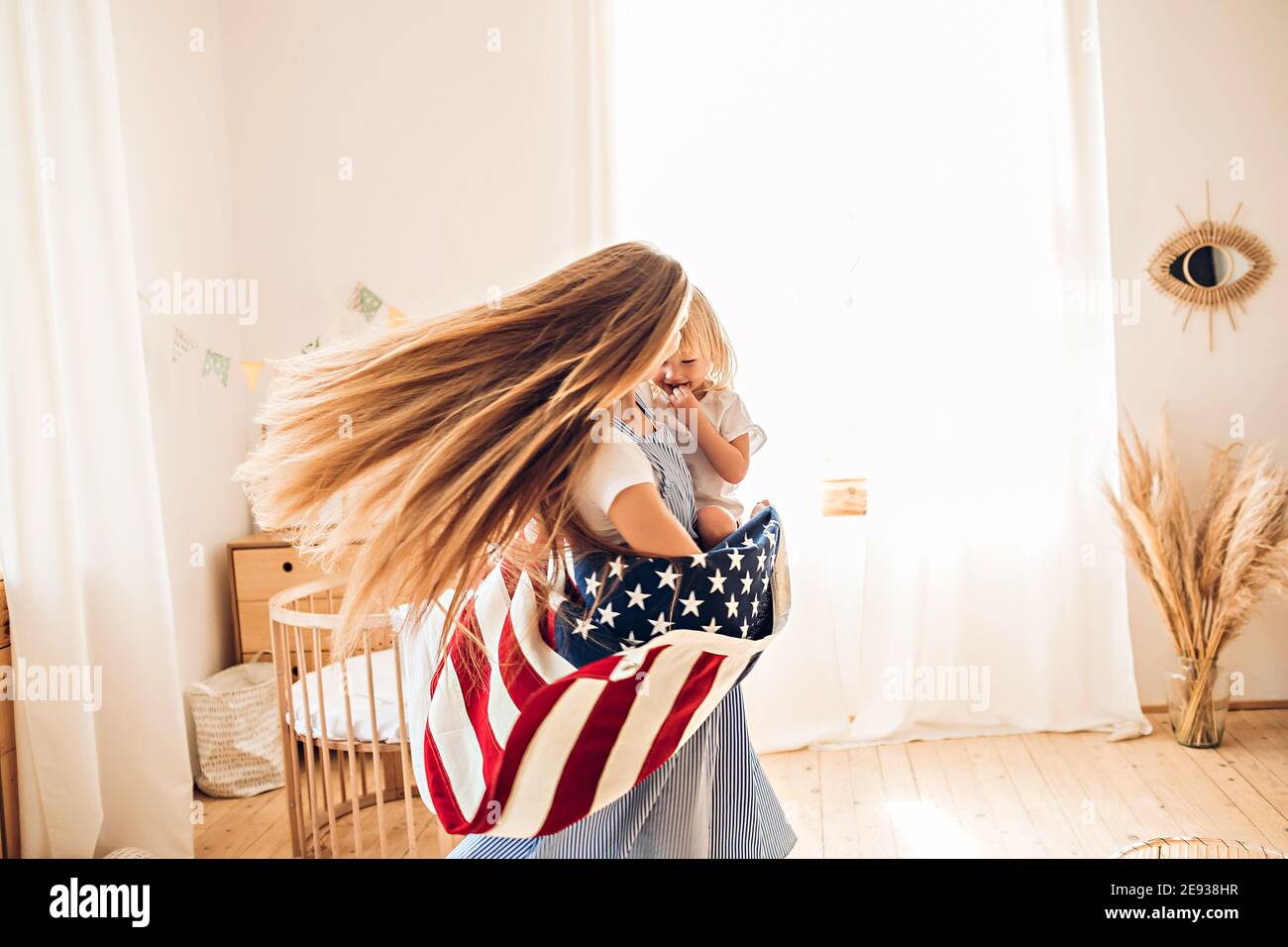 Junge Mutter oder Babysitter mit einem kleinen Mädchen in ihr Die Arme drehen sich in der Mitte des Raumes, um den Juli zu feiern 4th Unabhängigkeitstag Stockfoto