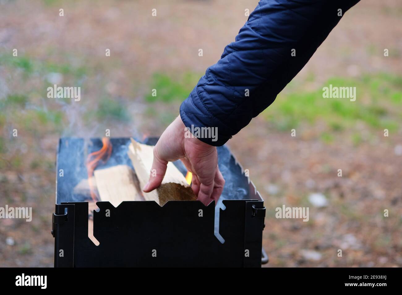 Beleuchtung des Grills. Der Mensch entzündet Feuer zum Grillen. Die Hand des Menschen fügt Holz ins Feuer. Stockfoto