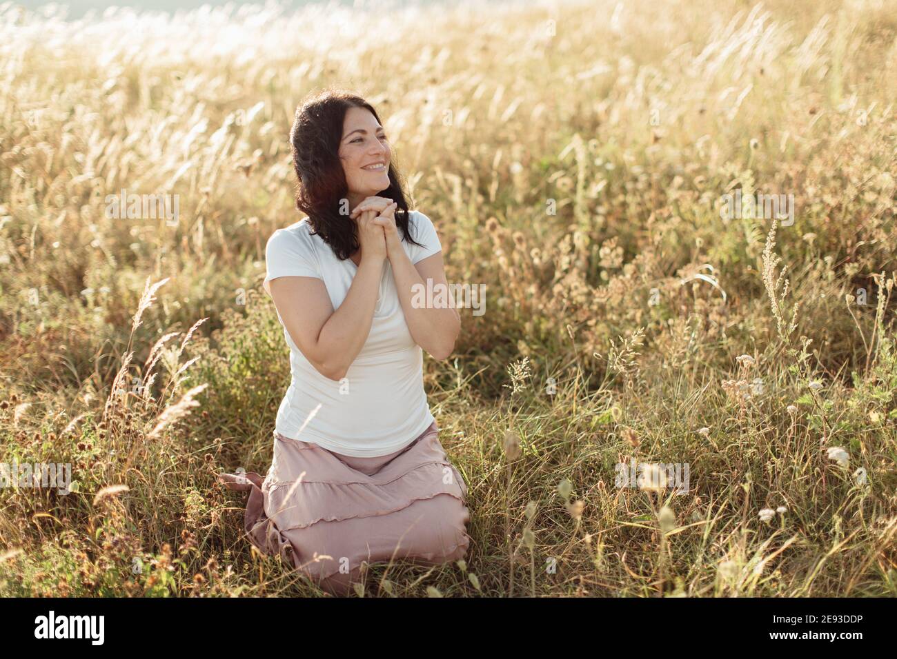 Glückliche Frau mit einem großen Lächeln kniet im Gras Stockfoto