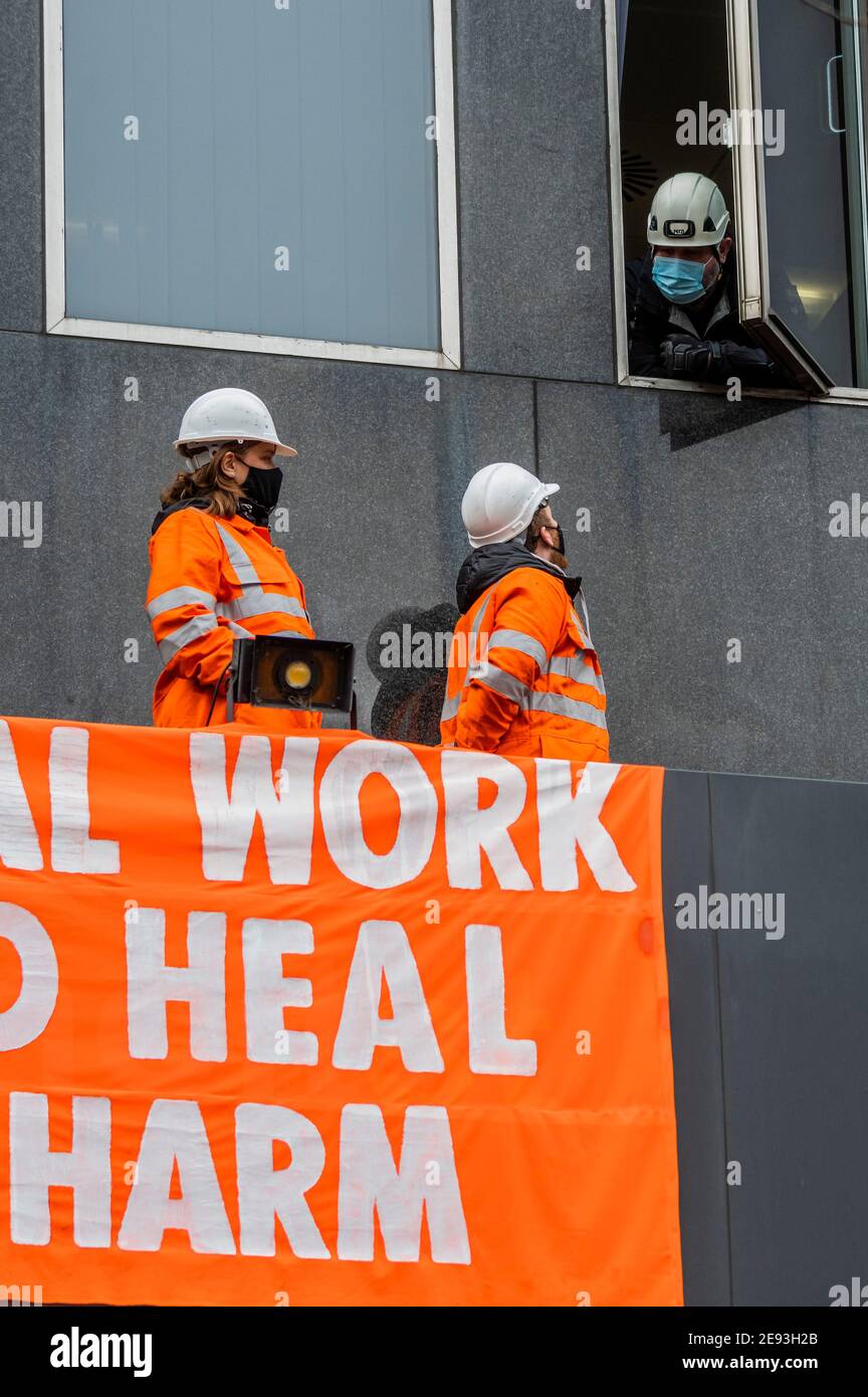 London, Großbritannien. Februar 2021. Die Polizei versucht, von einem Bürofenster aus zu verhandeln - Supporters from Extinction Rebellion inszenieren einen Protest auf dem Vordach über dem Eingang zur 0ne Everrsholt Street. Die londoner Zentrale von HS2- Sie haben ein Banner, das sagt, wesentliche Arbeit sollte Heilen nicht schaden. Das Anti-HS2-Lager für die Extinktion wird weiterhin von Gerichtsvollzieher (vom National Enforcement Team, NET, einer Tochtergesellschaft der High Court Enforcement Group) auf der Euston Station geräumt (um einen temporären Parkplatz zu schaffen). Kredit: Guy Bell/Alamy Live Nachrichten Stockfoto