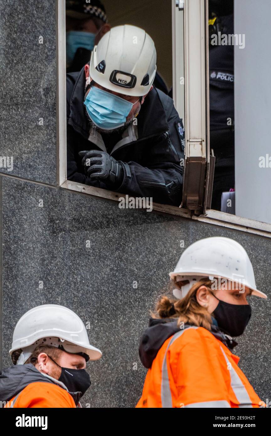 London, Großbritannien. Februar 2021. Die Polizei versucht, von einem Bürofenster aus zu verhandeln - Supporters from Extinction Rebellion inszenieren einen Protest auf dem Vordach über dem Eingang zur 0ne Everrsholt Street. Die londoner Zentrale von HS2- Sie haben ein Banner, das sagt, wesentliche Arbeit sollte Heilen nicht schaden. Das Anti-HS2-Lager für die Extinktion wird weiterhin von Gerichtsvollzieher (vom National Enforcement Team, NET, einer Tochtergesellschaft der High Court Enforcement Group) auf der Euston Station geräumt (um einen temporären Parkplatz zu schaffen). Kredit: Guy Bell/Alamy Live Nachrichten Stockfoto