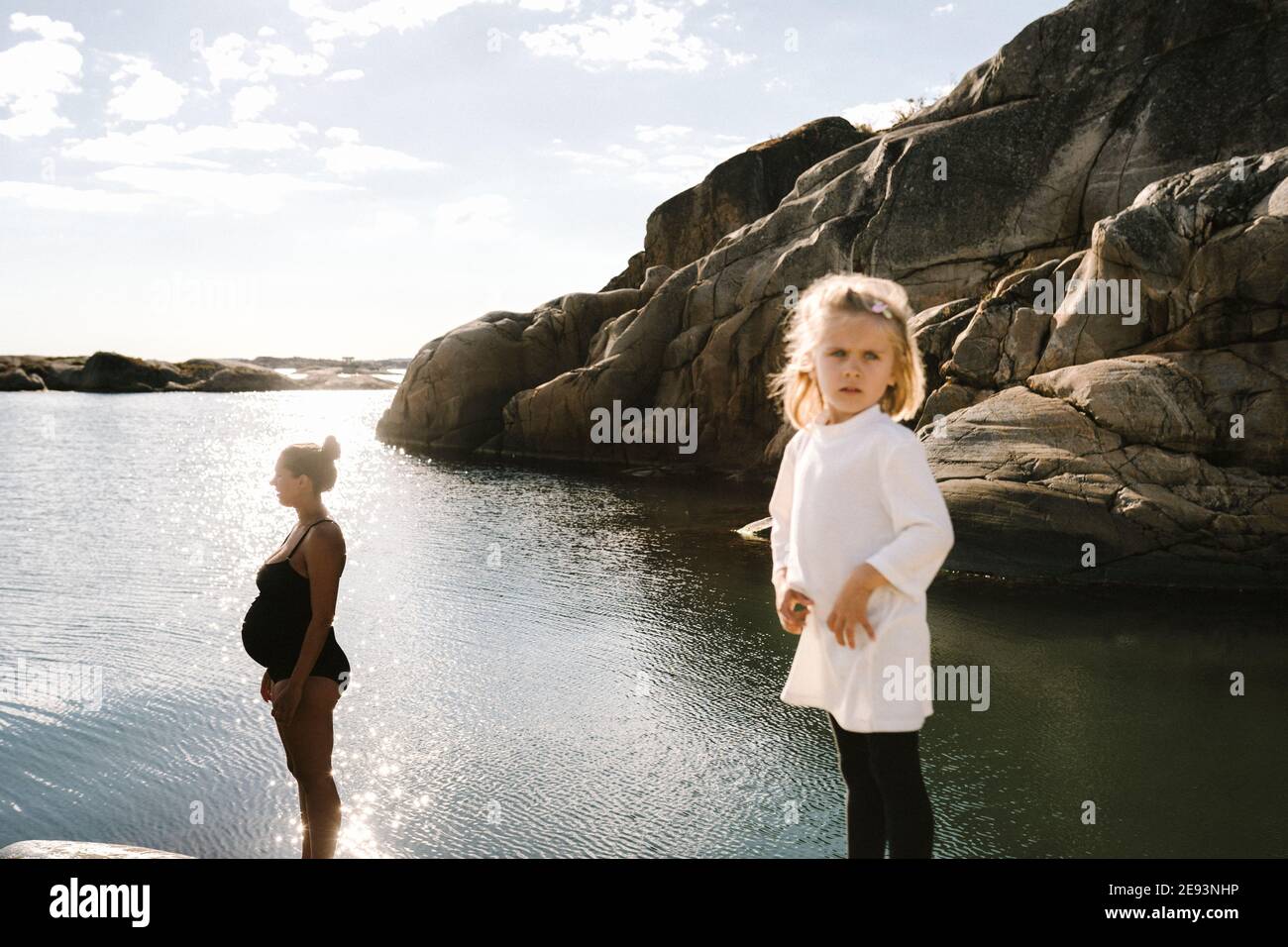 Mädchen auf See, schwangere Mutter im Hintergrund Stockfoto