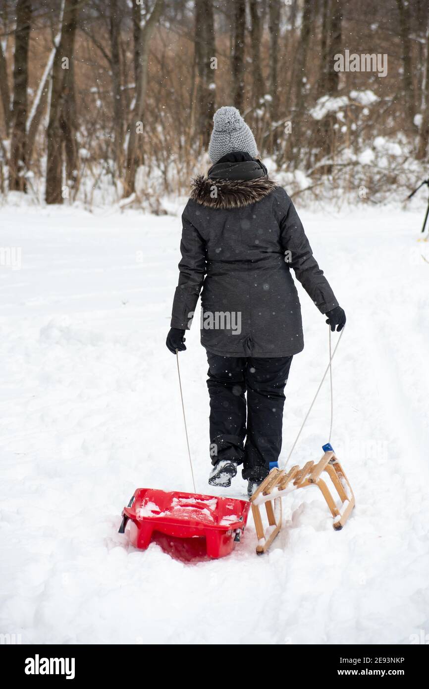 Mutter oder Mädchen oder Frau, die im Winter im Wald mit Schlitten und weißer Winterlandschaft im Hintergrund, vertikal Stockfoto