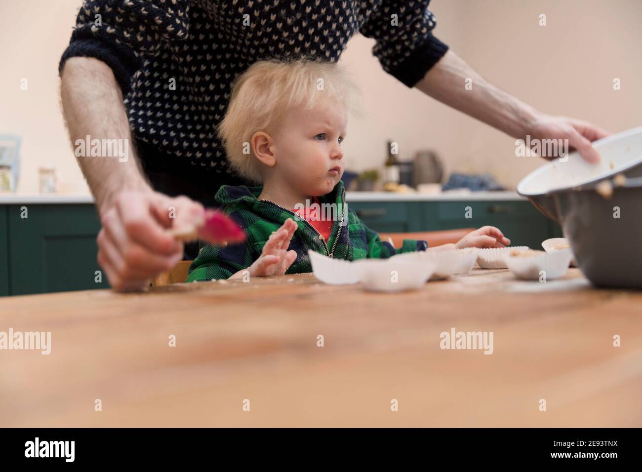 Ein junges Kleinkind hat Spaß dabei, seinem Vater beim Backen von Kuchen in der Küche zu helfen. Stockfoto