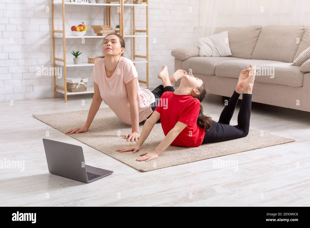 Covid Lockdown-Sport. Teen Mädchen und ihre Mutter tun Yoga Flexibilität Posen zu Video Tutorial Kurs zu Hause Stockfoto