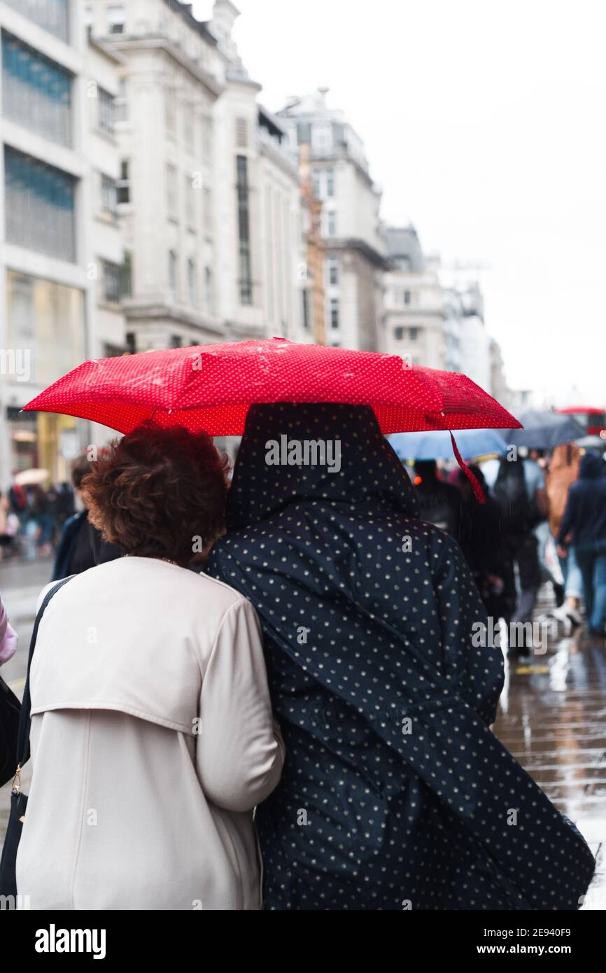 Rückansicht von zwei jungen Frauen unter dem Schirm während Ein Regen Stockfoto