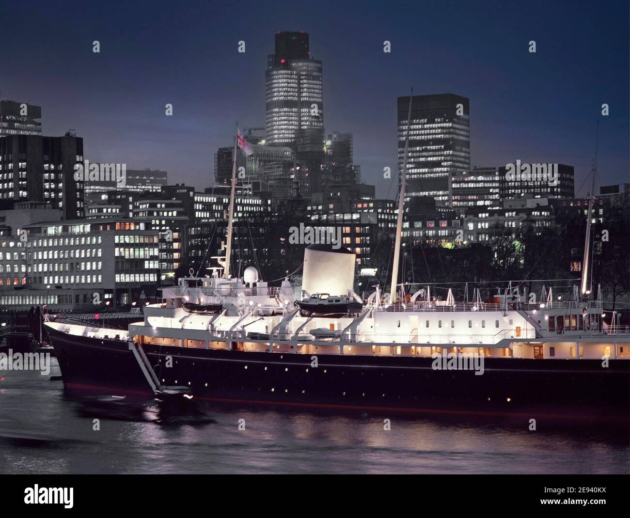 Historische Archivbilder auf der Hafenseite der Royal Yacht Britannia, die in der Abenddämmerung in der Themse am Pool von London im Jahr 1980s angedockt und mit Flutlicht beleuchtet wurde, mit der Skyline der City of London Nat West Tower Wahrzeichen Wolkenkratzer in der Art, wie wir England im Jahr 80s waren Stockfoto