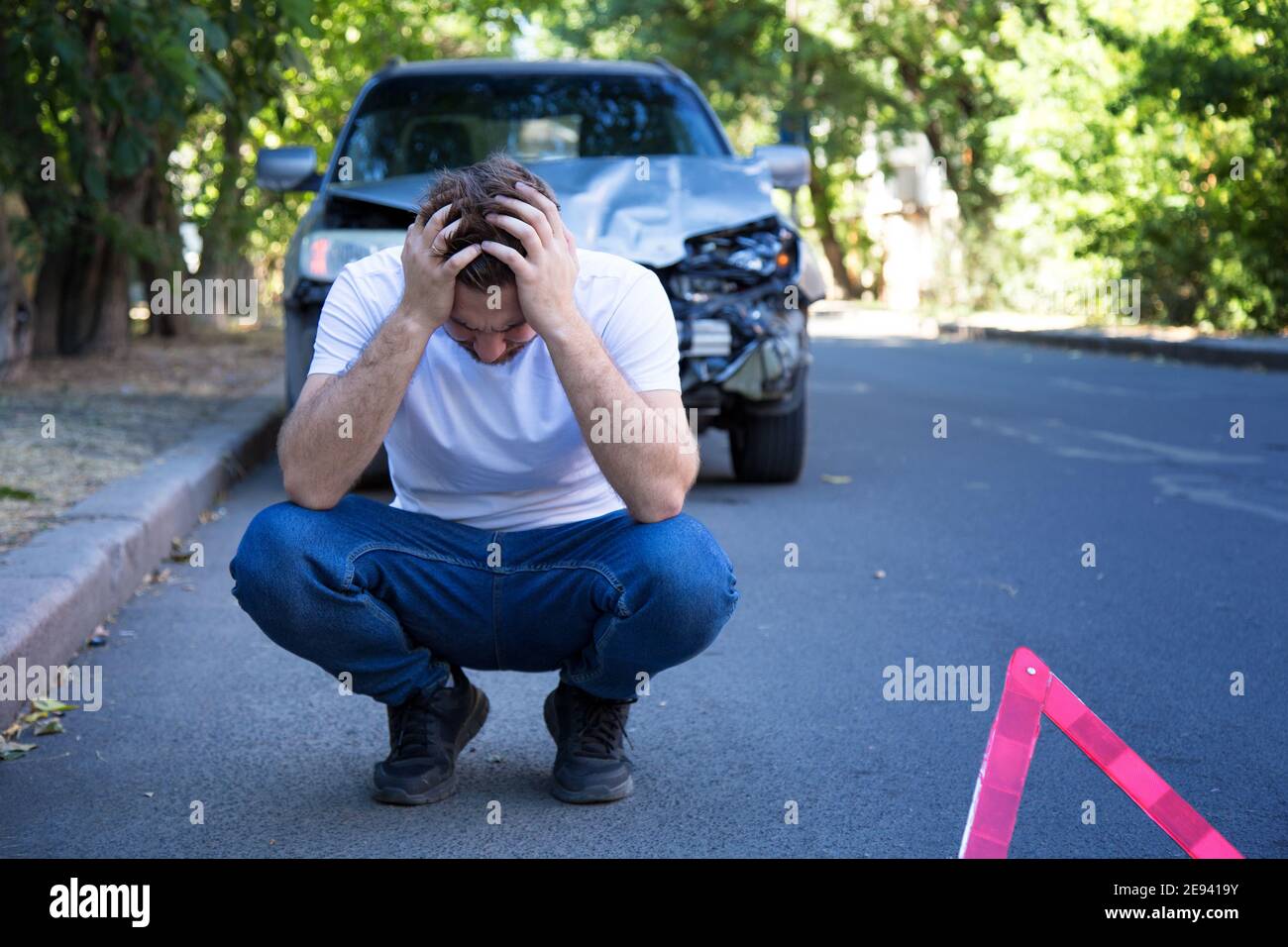 Fahrer Mann vor dem zerstörten Auto bei einem Autounfall. Verängstigte Mann hält seinen Kopf nach dem Autounfall. Tragische Autounfall. Gefährlicher Straßenverkehr Stockfoto