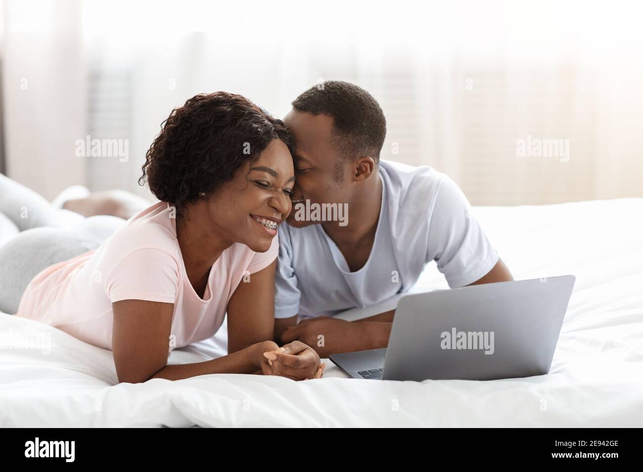 Junge nette afrikanische Paar mit Laptop, während im Bett ruhen Stockfoto
