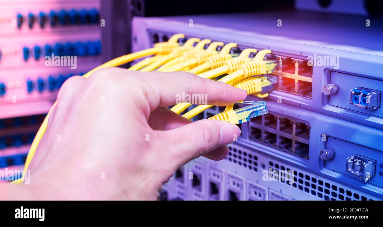 Hand, die Netzwerkkabel auf dem Switch Hub im Server raum Hintergrund Stockfoto