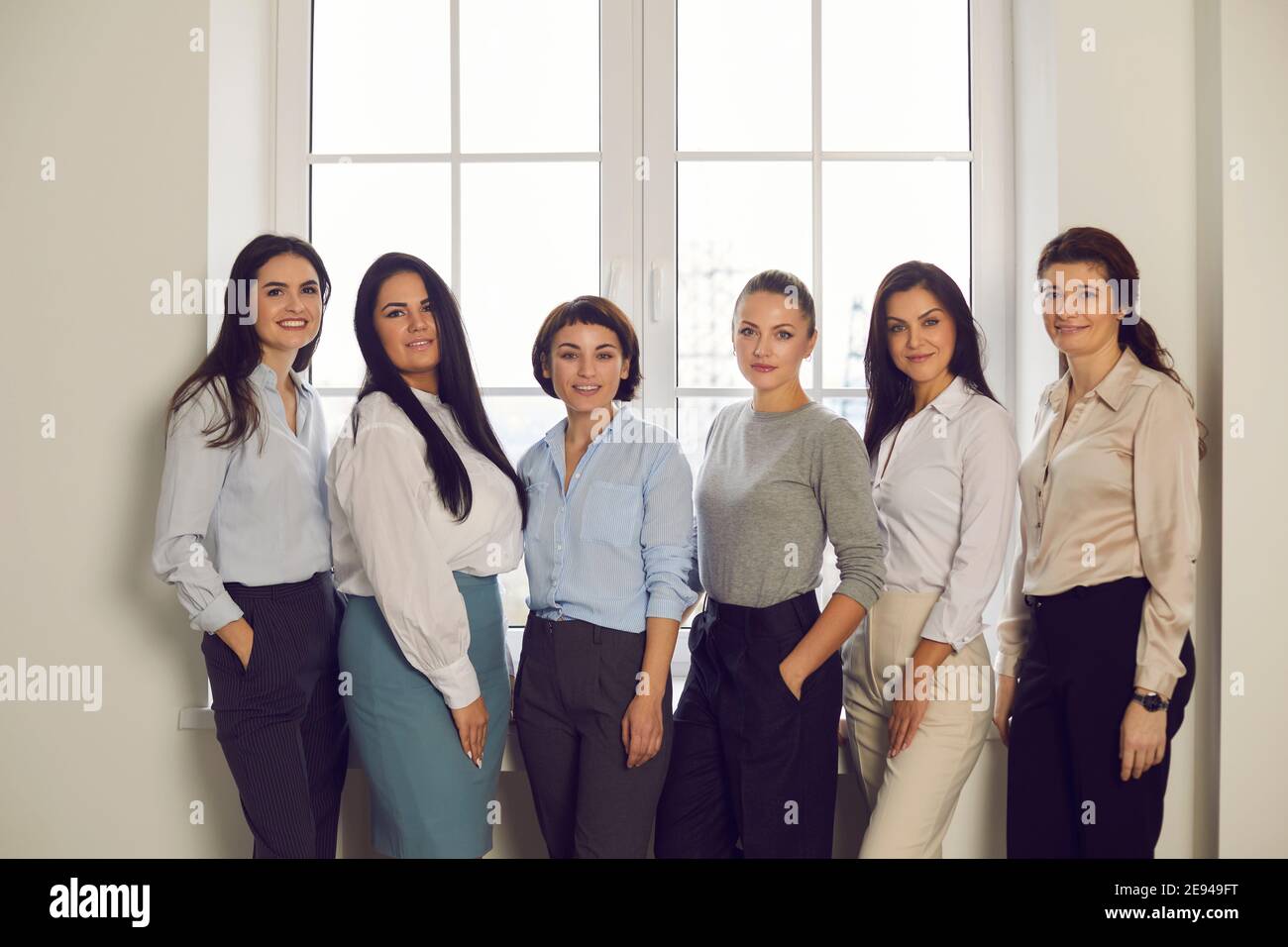 Team von selbstbewussten Geschäftsfrauen stehen am Bürofenster und Lächelnd in die Kamera Stockfoto