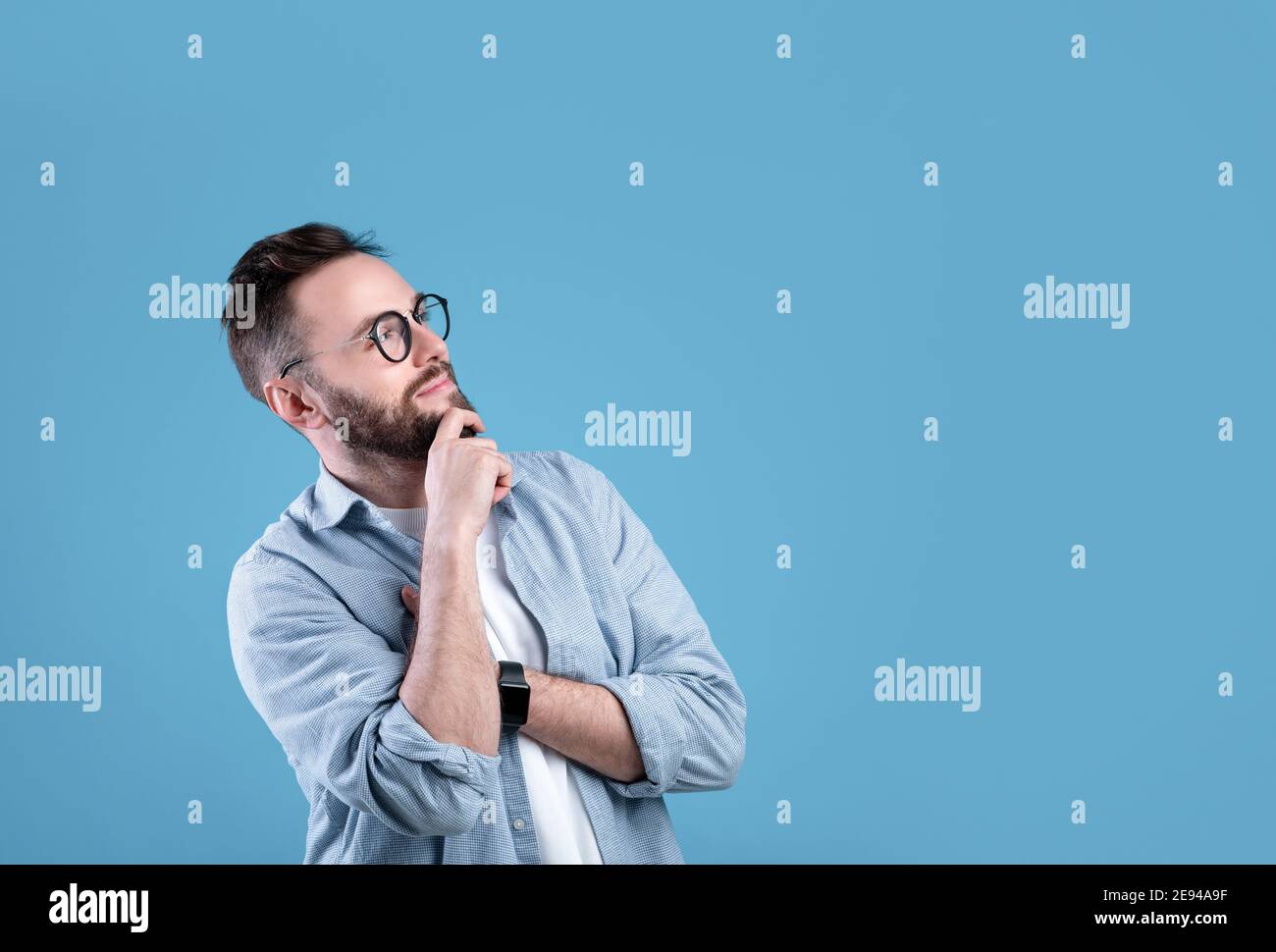 Nachdenklicher kaukasischer Kerl, der über Entscheidung oder Problem nachdenkt, mit Blick auf leeren Raum über blauem Studiohintergrund Stockfoto