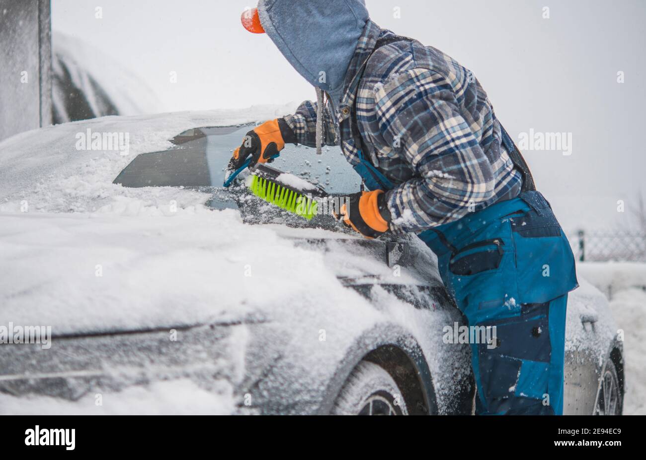Kaukasische Männer Entfernen Schnee von seinem modernen Sportback Fahrzeug und Enteisung Front Windschutz. Automotive Winter Matinenance. Stockfoto