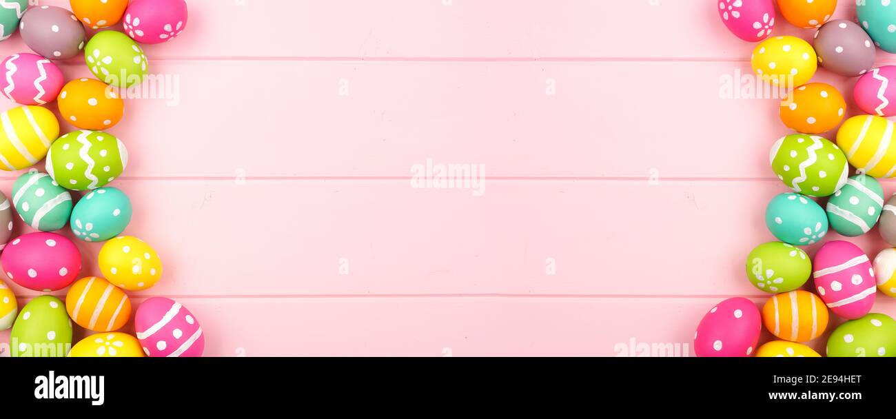 Farbenfrohes Osterbanner mit doppelseitigem Ostereierrand vor einem rosa Holzhintergrund. Draufsicht mit Kopierbereich. Stockfoto