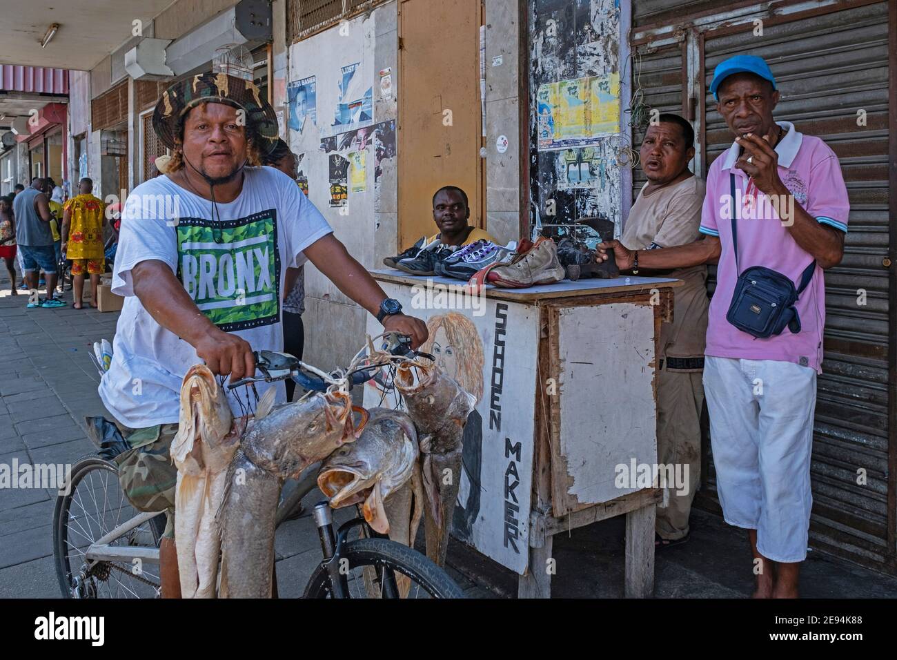Verkauf von großen Fischen von einem Fahrrad und einem kleinen Schuhreparaturstand im Zentrum von Paramaribo, Surinam. Stockfoto