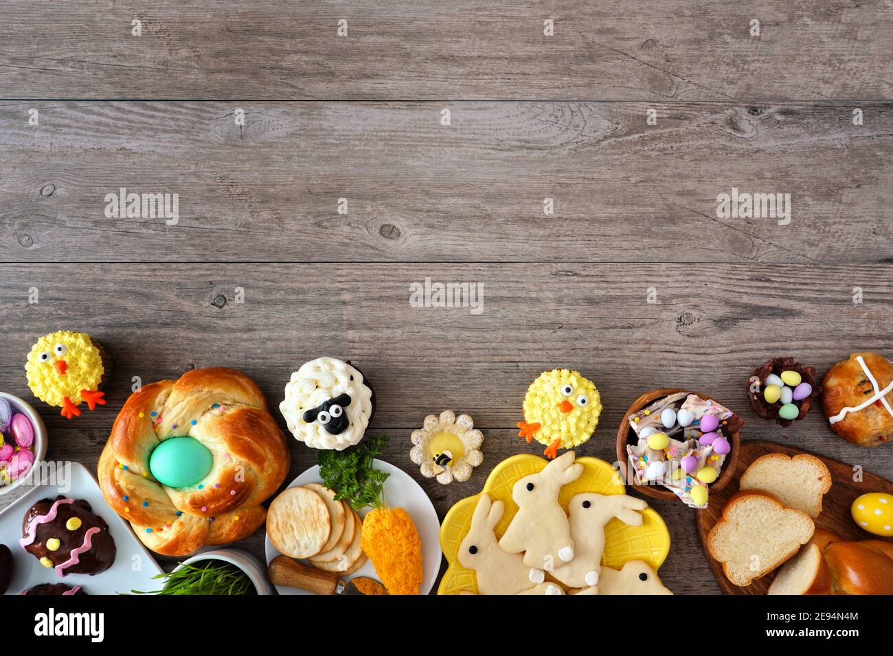 Ostertisch-Szene mit einer Auswahl an Broten, Desserts und Leckereien. Draufsicht unterer Rand über einem Holzhintergrund. Frühlingsurlaub Essen Konzept. Stockfoto