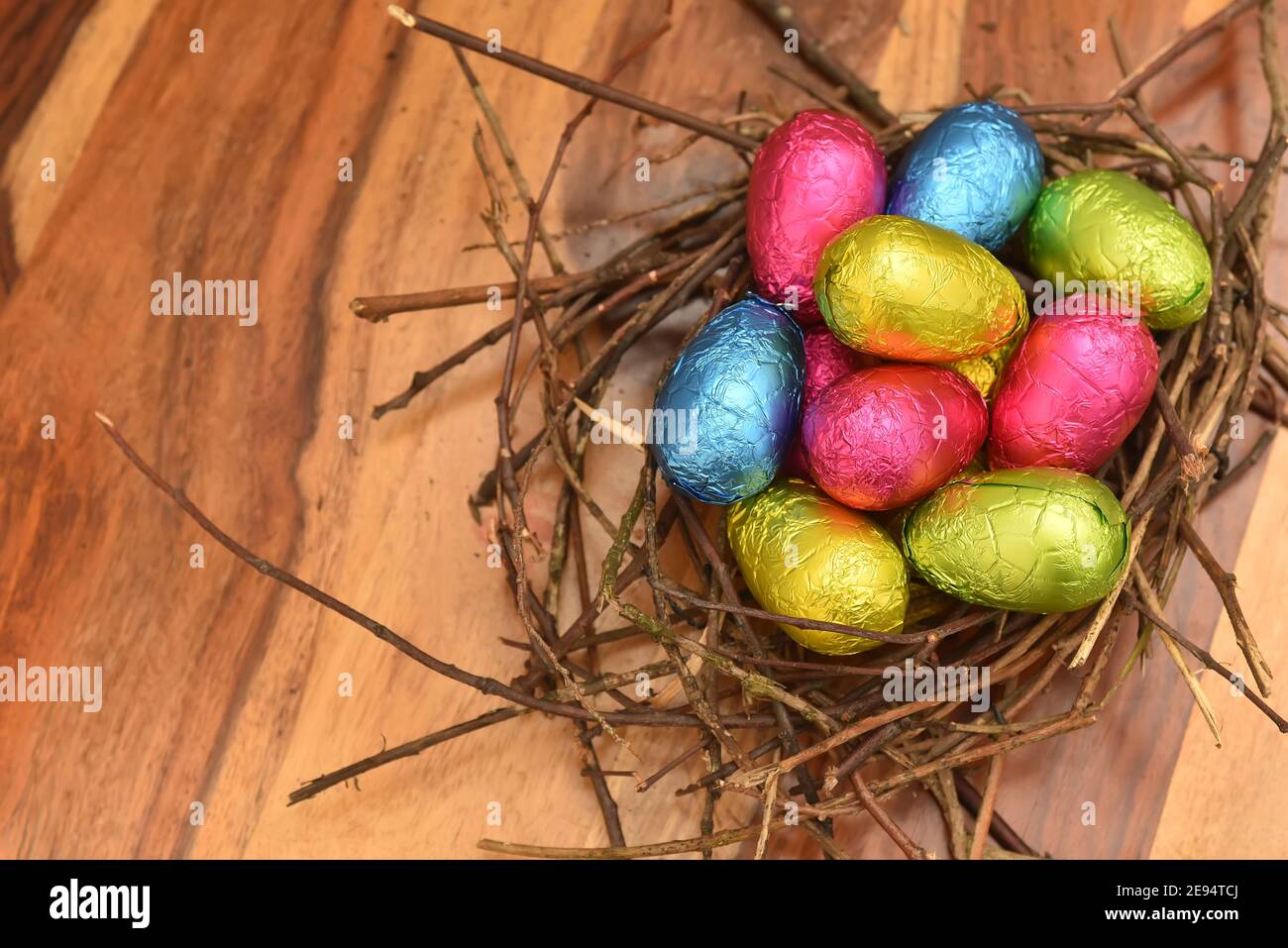 Foliengewickelte bunte ostereier in rosa, grün, blau und gelb in einem natürlichen Nest aus Stäben und Zweigen, gegen einen mehrkörnigen braunen Holzhinterst Stockfoto