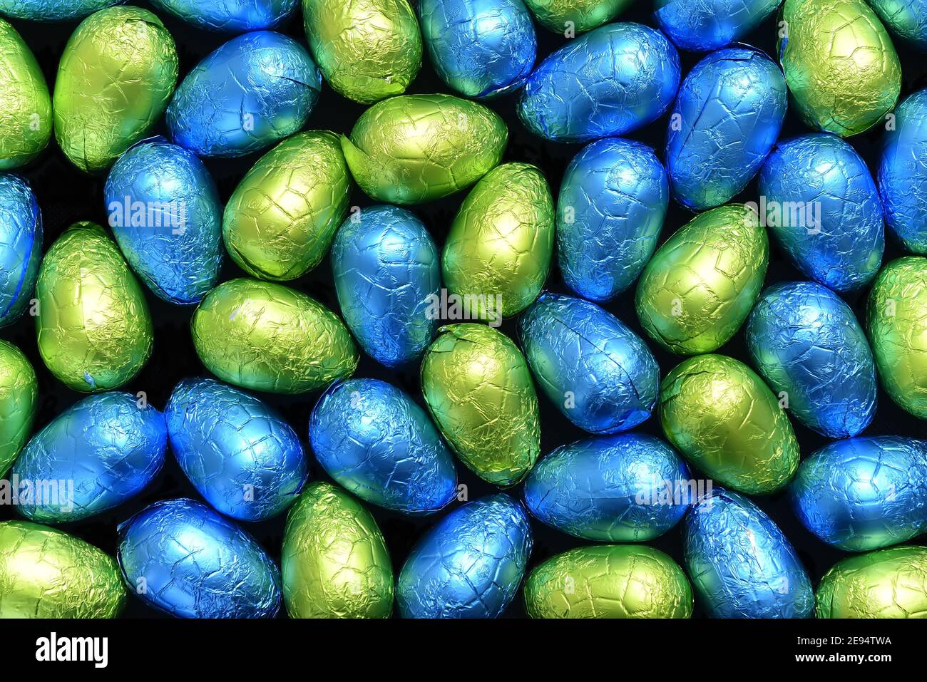 Stapel oder Gruppe von mehrfarbigen und verschiedenen Größen von bunten Folie verpackt Schokolade ostereier in blau, gelb und lindgrün. Stockfoto