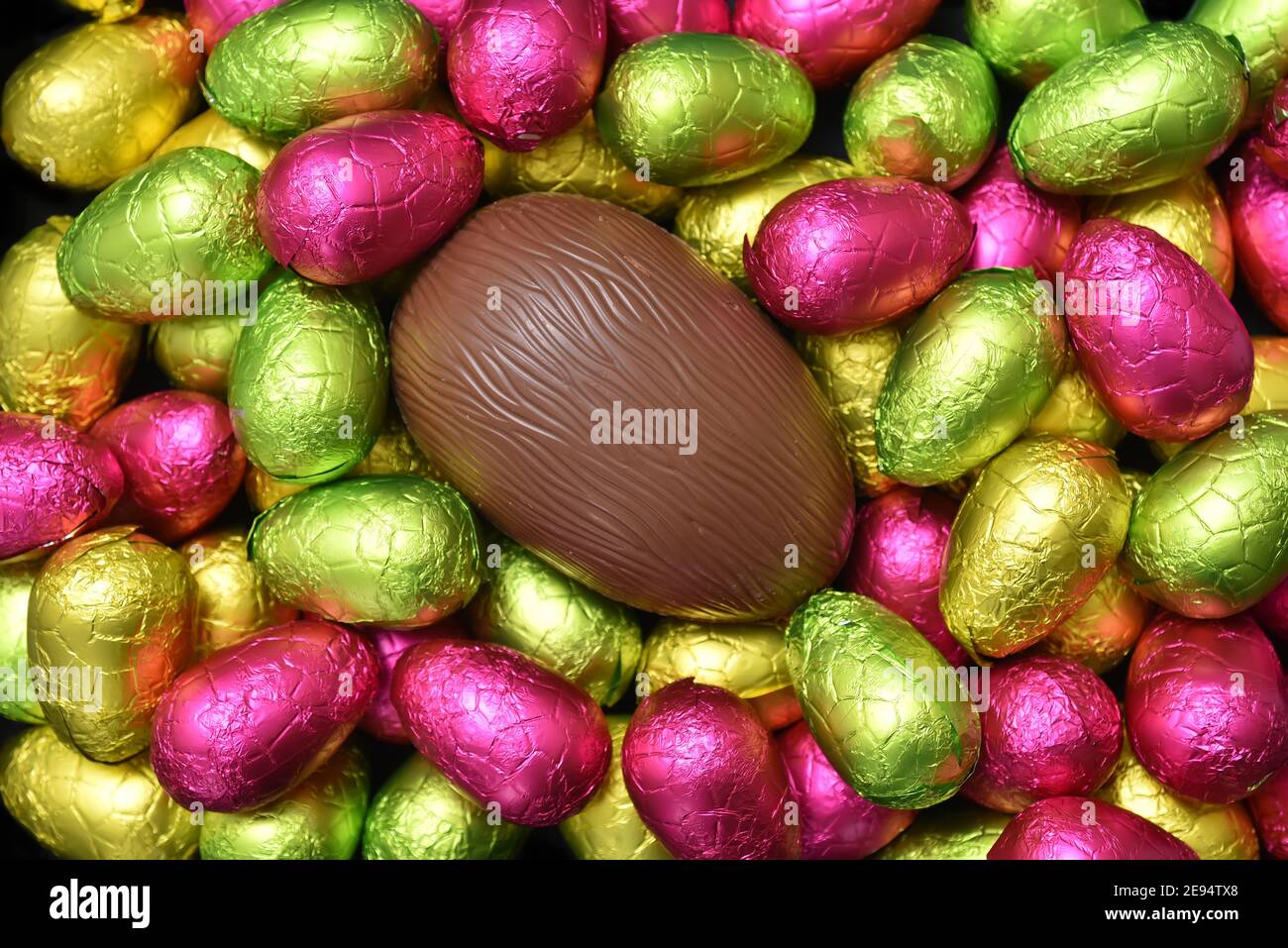 Stapel oder Gruppe von mehrfarbigen und verschiedenen Größen von bunten Folie verpackt Schokolade ostereier in rosa, rot, gelb und lindgrün. Stockfoto