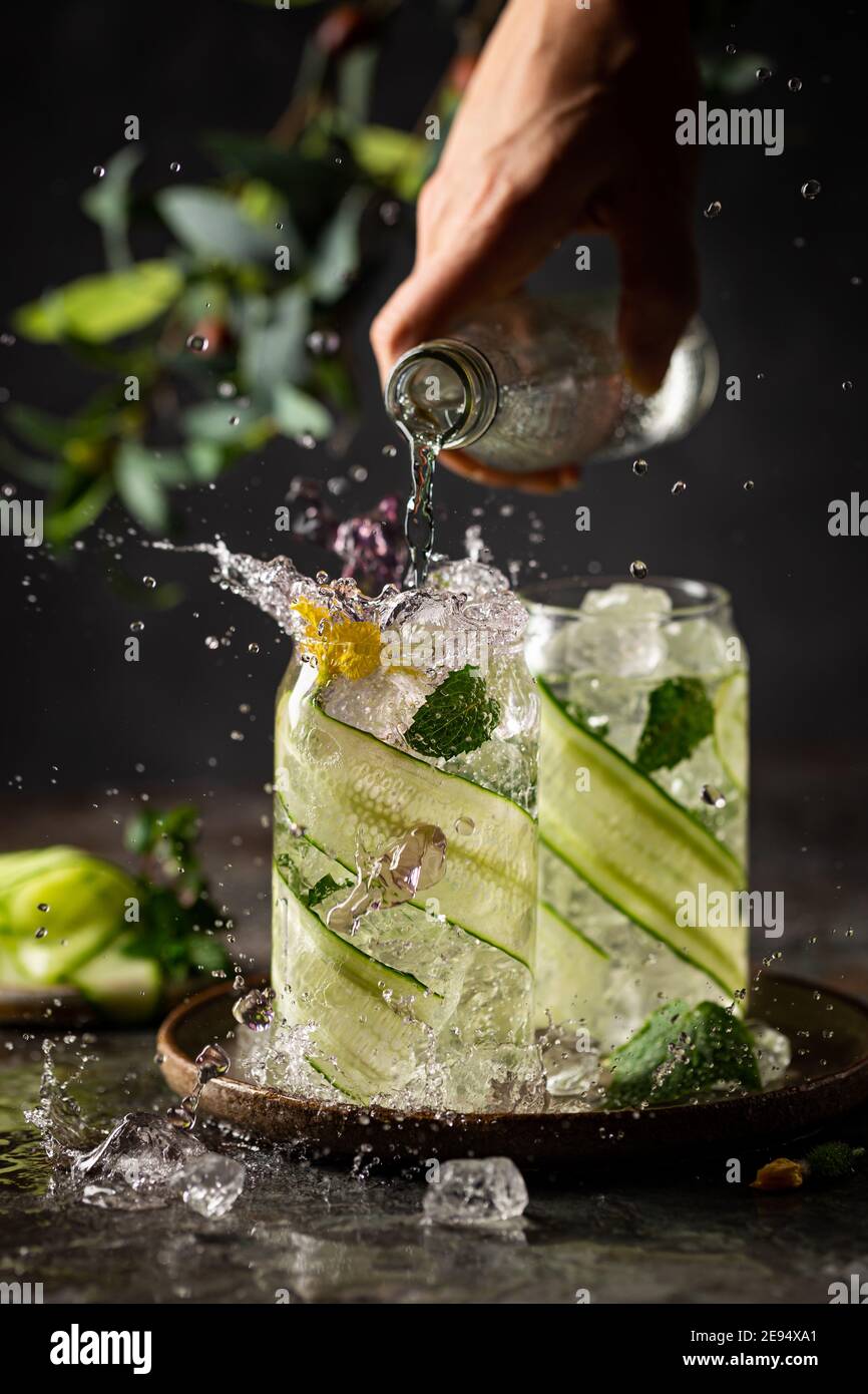 Gurke in ein Glas mit Eis eingegossen Detox-Wasser mit Minze. Levitation von Gurkengetränk auf dunklem Hintergrund Stockfoto