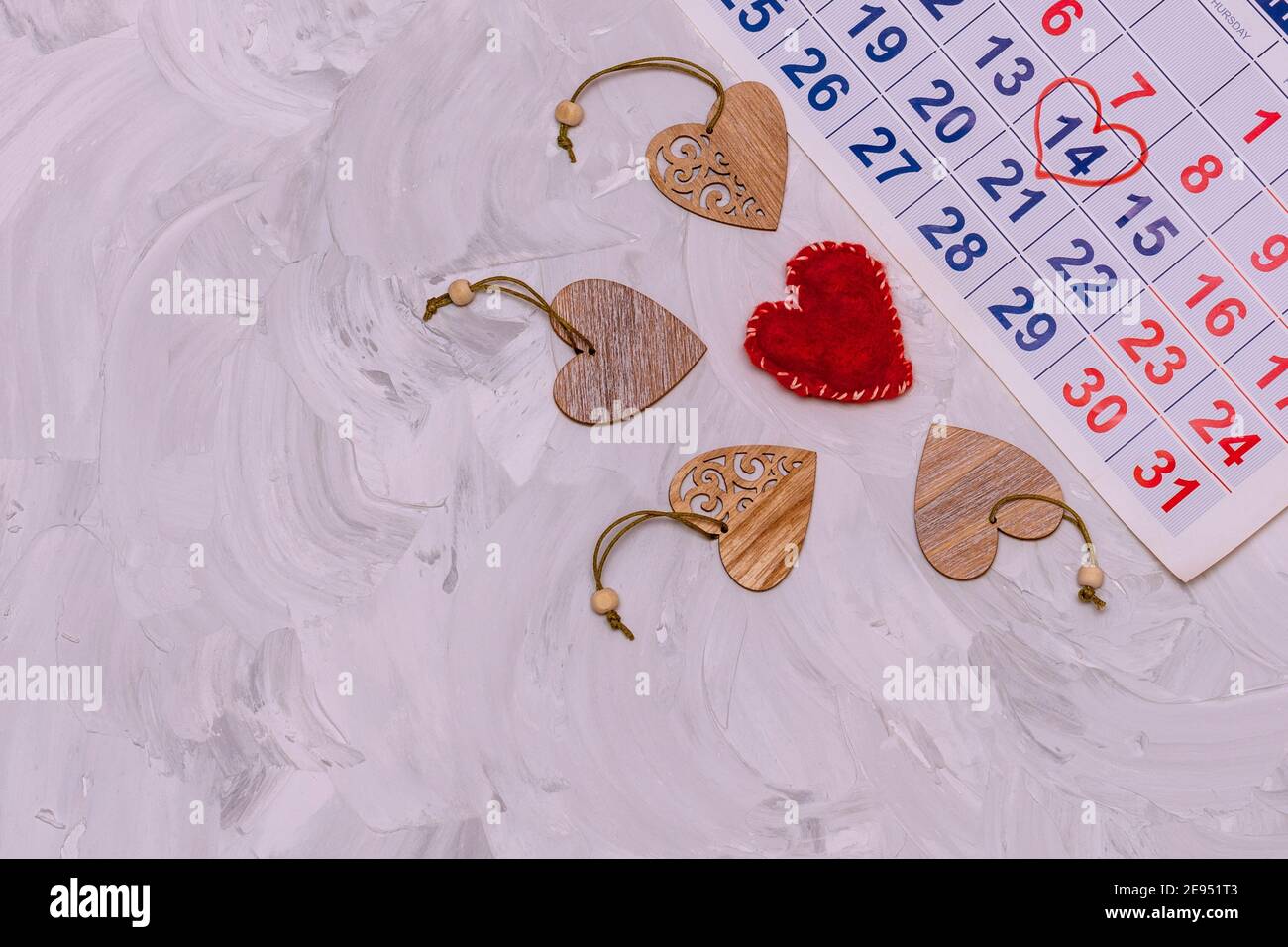 Blatt Wandkalender mit Datum Februar 14th markiert. Rotes Herz aus Wolle und viele Herzen aus Holz mit Ornamenten geschnitzt. Komposition für Vale Stockfoto