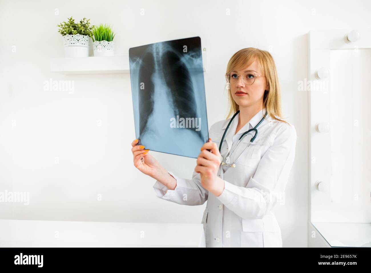 Attraktive Ärztin im weißen Mantel, mit einem Stethoskop am Hals hält eine Röntgenaufnahme in den Händen.Untersuchung von Patienten mit Coronovirus, viral Stockfoto