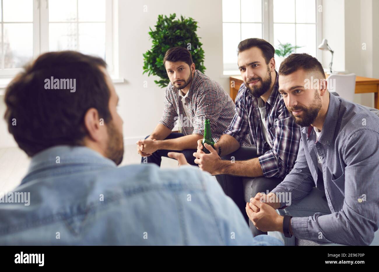 Gruppe junger Männer, die auf dem Sofa sitzen, Bier trinken und der Geschichte ihres Freundes zuhören Stockfoto
