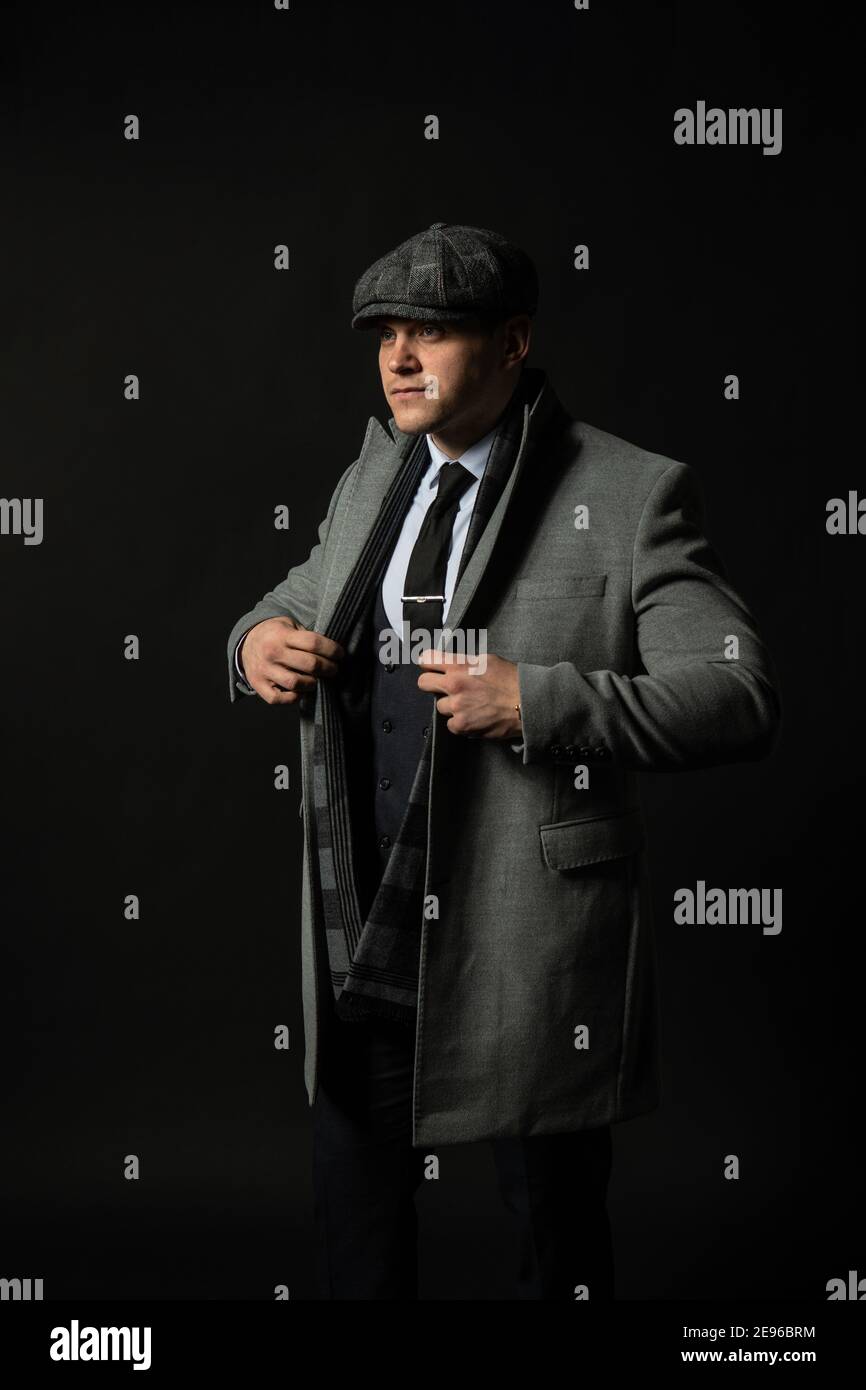 In einem Mantel und einer Mütze ein Schal junger Mann drei Stück Anzug smart, Porträt eines trendigen Kerl, erfolgreiche Eleganz Hintergrund schwarz Bodybuilder Stockfoto
