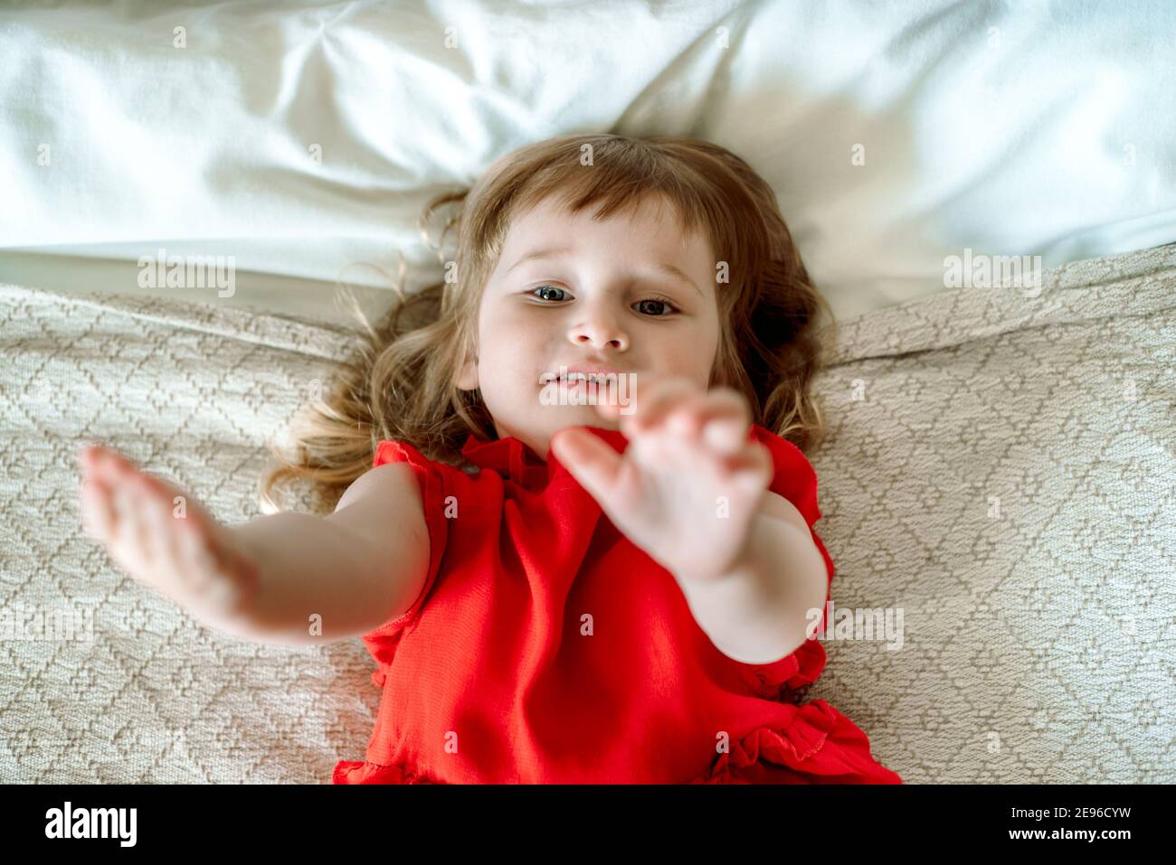 Baby Mädchen hält ihre Hände mit einer Anfrage Top View. Schlechte Laune, weint und fragt, besteht und fordert. Liegend auf dem Bett. Bittet um Hilfe, Stockfoto
