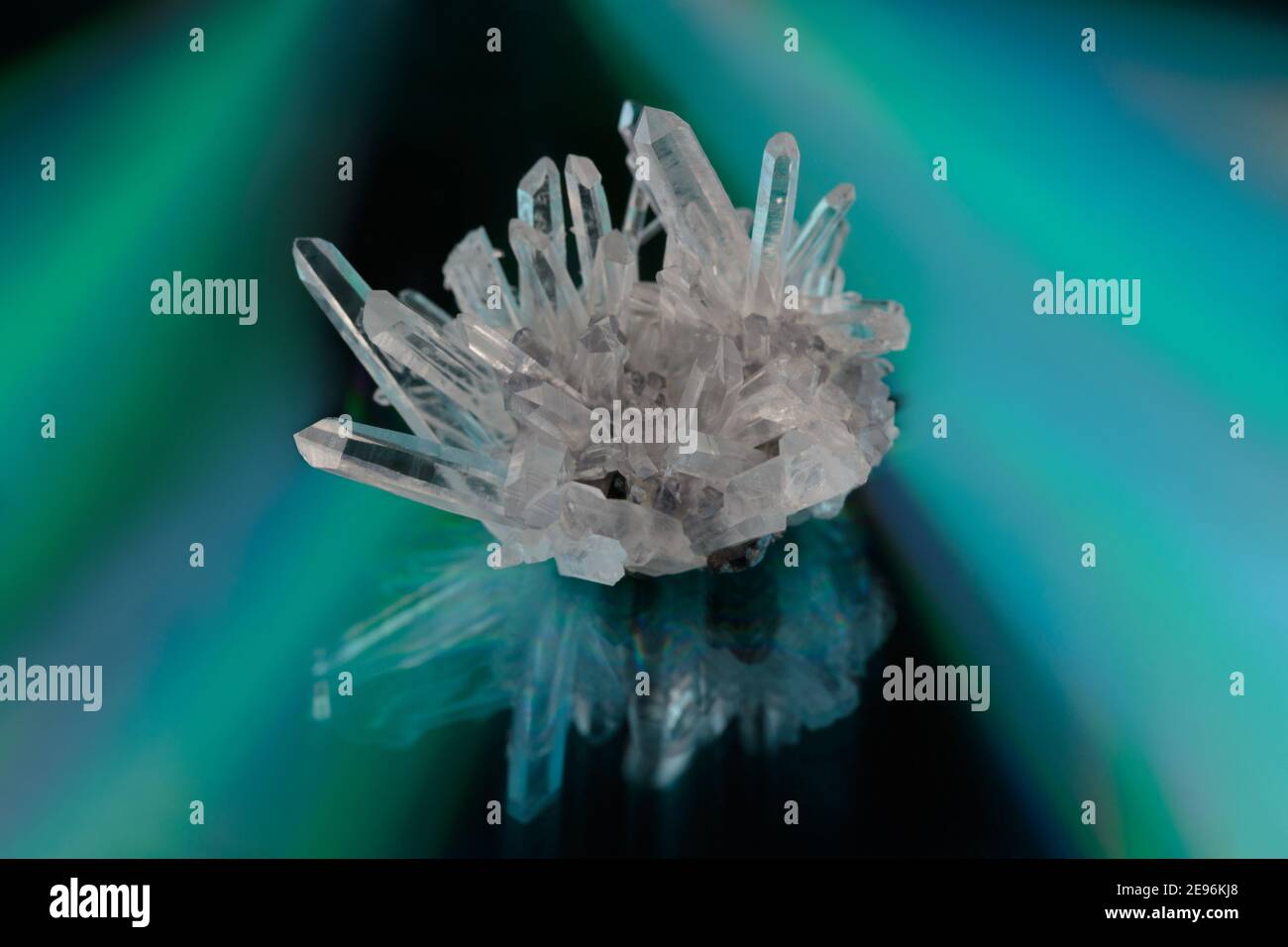 Ein Cluster von rohen klaren Quarzkristallen auf einem reflektierenden, irisierenden Hintergrund, der dreieckige Farbverläufe in Grün, Türkis und Violett erzeugt, Kopierraum Stockfoto