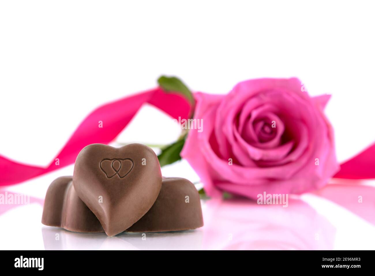 Drei herzförmige Pralinen und rosa Rose auf weißem Hintergrund. Valentinstagskonzept, selektiver Fokus. Stockfoto