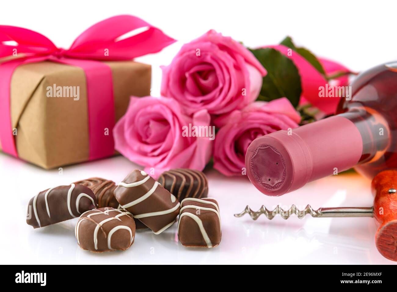 Valentinstag-Konzept. Köstliche Schokoladen-Pralinen, Weinflasche, Korkenzieher, rosa Rosen und Geschenkbox auf weißem Hintergrund. Selektiver Fokus. Stockfoto