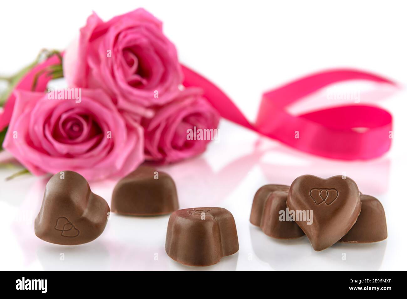 Herzförmige Pralinen und Bouquet von rosa Rosen auf dem weißen Hintergrund. Valentinstag und Frauentag Konzept, selektiver Fokus. Stockfoto