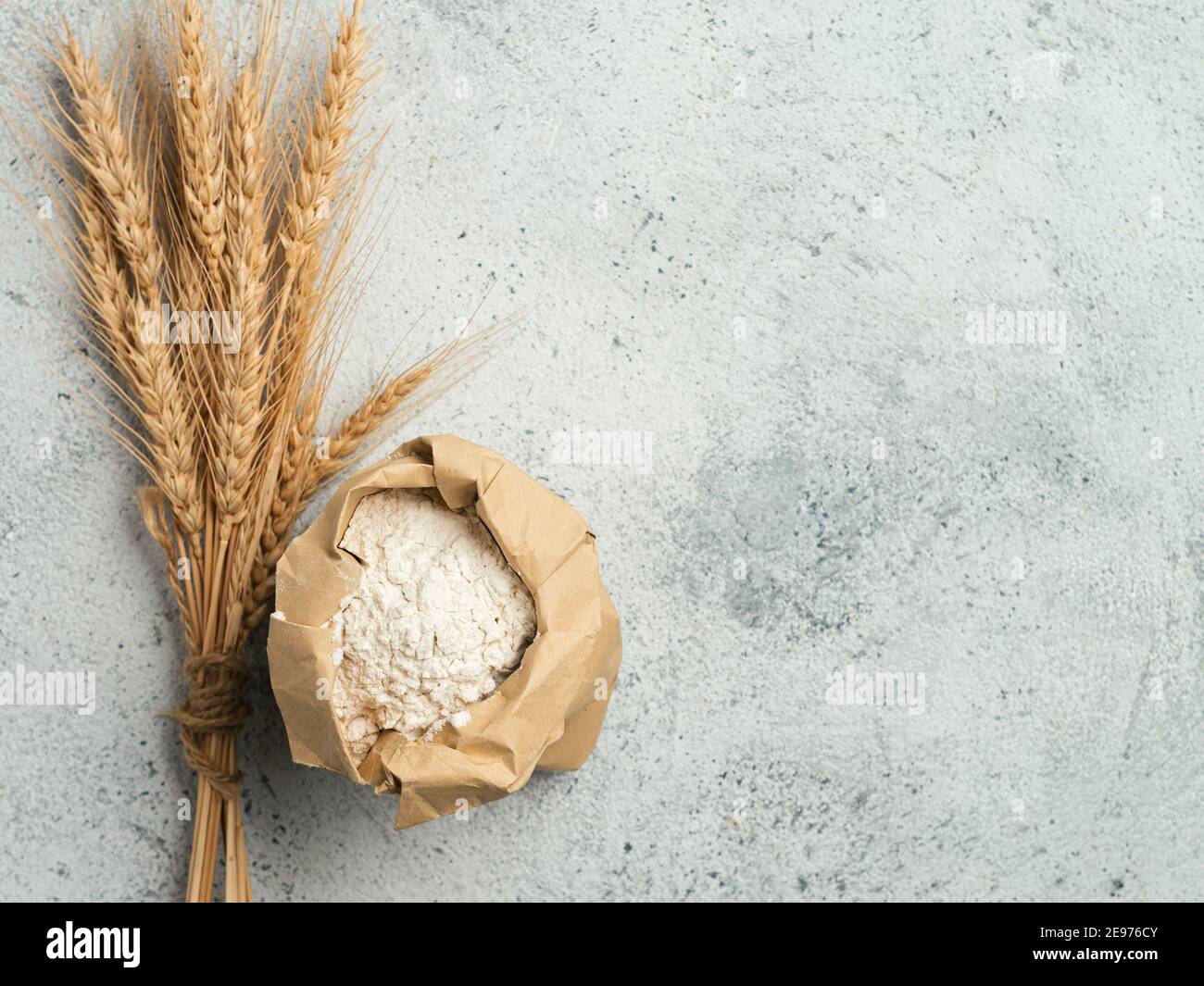 Weizenmehl in Papiertüte und Spikes über grauem Zement Hintergrund. Lebensmittel und Backzutat - Allzweckmehl mit Kopierfläche Stockfoto