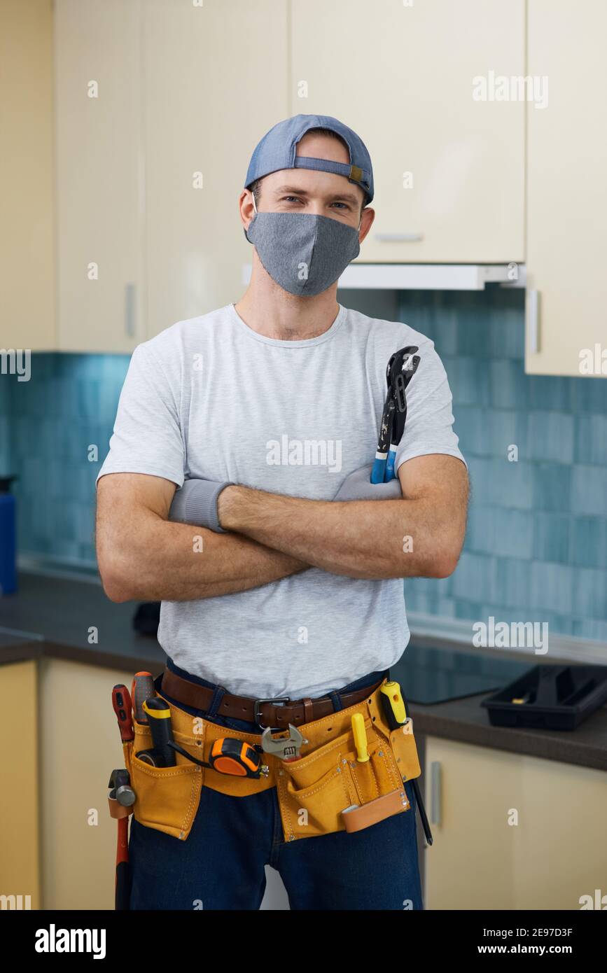 Ich repariere es. Professionelle Werkstatt trägt eine Maske und ein Werkzeug Gürtel Blick auf Kamera und stehen mit Armen gekreuzt, während immer bereit für die Befestigung eines Waschbecken Stockfoto